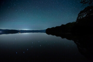 星の煌めく夜空を湖面に反射する夜の湖