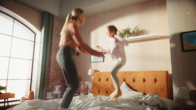 Mother and Small Daughter Having Fun at Home. Cheerfully Playing, Running Around and Jumping on a Bed in Stylish Loft Apartment. Happy Childhood, Parenthood and Motherhood Memories.