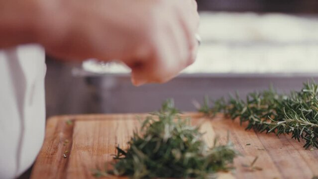Close-up shot of male hands cutting fresh green rosemary on wood chopping board, slow motion