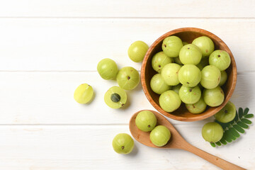 Flat lay of Fresh Amla (Indian gooseberry) fruits in wooden bowl on white wood.