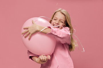 horizontal portrait of a cute, beautiful, happy girl with blond hair hugging a big balloon standing in a pink dress on a pink background with an empty space for an advertising tex