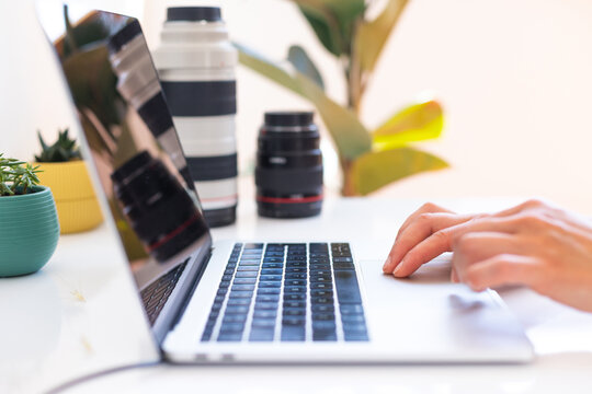 Photographer's workplace, laptop and camera lenses on a white table, hands on keyboard close up