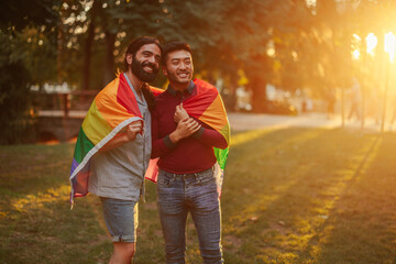 Same sex couple hug with pride flag in city