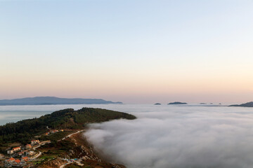 Fototapeta na wymiar Una lengua de tierra penetra en el mar cubierto por una densa niebla. Cabo Home, Morrazo, Galicia, España.