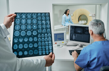 Radiographers analyzing results of CT scan of patient's head are found in control room at hospital...