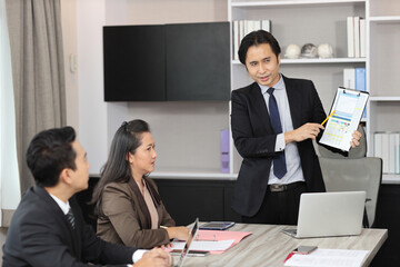 Collaborative process of young asian business people team working together discussing, researching, brainstorming and planning work at business meeting in modern office building and city background