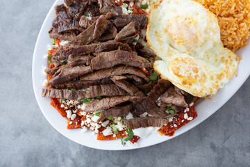 A top down view of a plate of a breakfast plate of carne asada and chilaquiles.