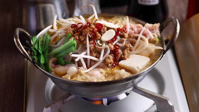煮え立つ出汁の中でプルプルと震える牛モツの、脂がのった柔らかな質感を閉じ込めた「モツ鍋動画」。熱々の湯気と濃厚な旨みの輝きが際立つシーンで、冬の宴会や居酒屋メニューの販促に最適な高品質素材です。 | Sizzling hot Motsunabe (offal pot) boiling with fresh vegetables.