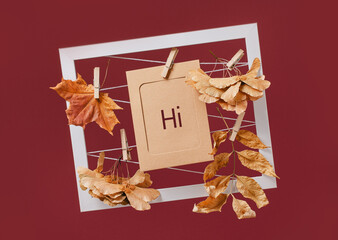 hi. hello text on card, Autumn fall composition with maple leaf and other leaves and in a frame on dark red maroon background
