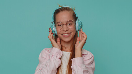 Happy pretty teenager relaxed girl in glasses listening music via headphones and dancing disco...