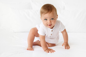 Funny blue-eyed baby crawling on white bed