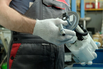 Car maintenance in a car service center. Repair of the fuel and exhaust system of the car. An auto mechanic holds a new fuel pump in his hands, controls its integrity.