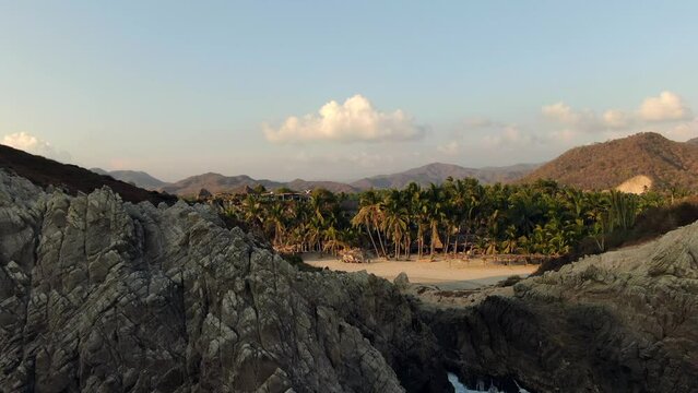 Lush Palm Trees And Waves Splashing On Huge Boulders At Playa Maruata On A Sunny Afternoon In Michoacan, Mexico. aerial drone pullback
