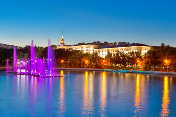 Fototapeta na wymiar Colorful Illuminated Fountains on the Svisloch River During Summer Night Against Blue Sky Night View of Minsk City Center and Famous National Landmark of Belarus.