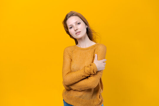 Smiling young female woman in yellow sweater posing isolated on pastel yellow background studio portrait. People sincere emotions lifestyle concept. Flow out onto copy place. Keeping your arms crossed
