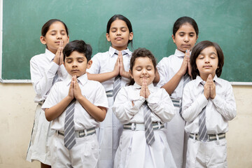 Group of indian elementary school kids join hands and offer prayer in class room.