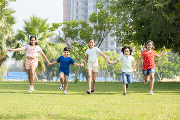 Group of happy playful Indian children holding each other hands running together outdoors in spring park. Asian kids Playing in garden.
