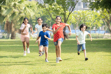 Group of happy playful Indian children running outdoors in summer park. Asian kids Playing in garden enjoy fun activity sport, holidays and vacations ,picnic, camp,  