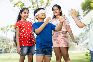 Group of happy Indian kids playing blindfold game outdoors in park, Playful asian children in the...