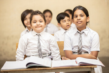 Indian elementary school students sitting at desk in classroom with textbook, Girl Education concept.