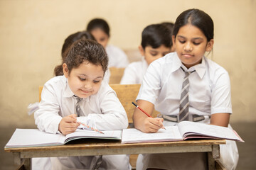 Indian elementary school students sitting at desk in classroom with writing in notebook with pencil, Examination and test, Girl Education concept.