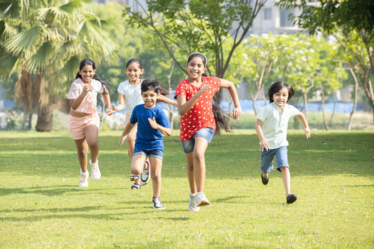 Group of happy playful Indian children running outdoors in spring park. Asian kids Playing in garden.