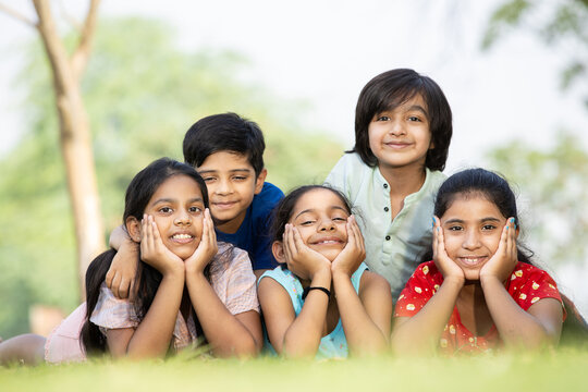 Group of happy Indian children lying on green grass outdoors in spring park, Playful asian kids in the garden.