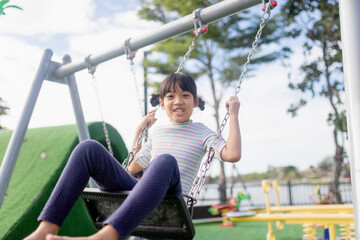 A little girl is having fun riding a swing.