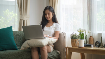 Happy young woman sitting on couch in living room and using laptop computer.
