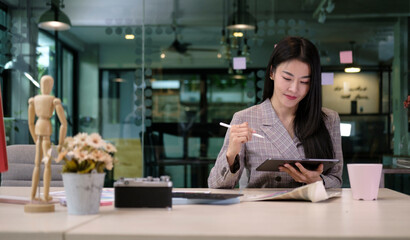 Attractive young businesswoman sitting in modern office and using digital tablet.