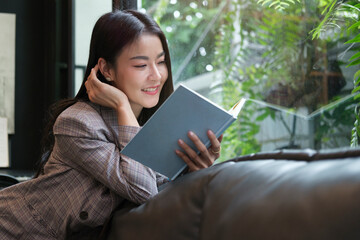 Positive businesswoman reading book while relaxing on couch in her office.
