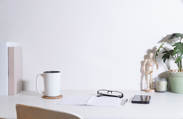 Comfortable workplace with coffee cup, smart phone, potted plant and stationery on white table.