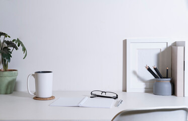 Office desk with picture frame, coffee cup, houseplant and supplies on white table. Copy space for your advertise text.