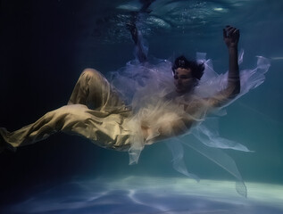 Fototapeta na wymiar young man in white ribbons and trousers underwater in the pool on a dark background