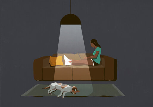 Dog sleeping on floor next to woman working late at laptop on sofa
