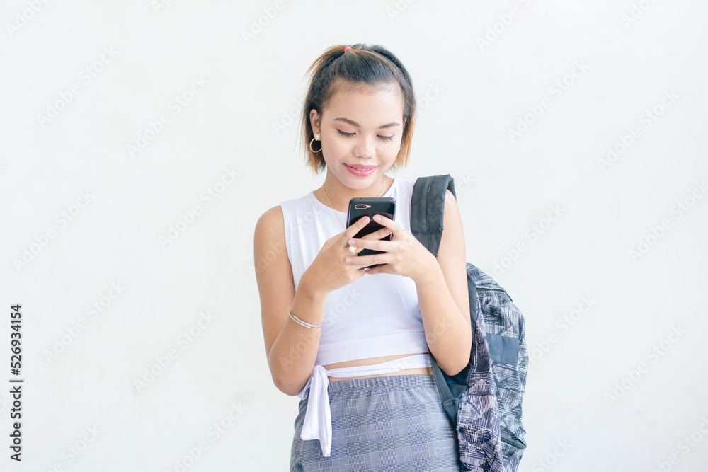 Wall mural A short haired student wearing a white sleeveless top and printed skirt sending a text message using her phone isolated on a white background - Wall murals
