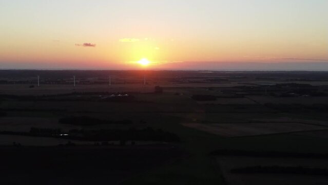 drone flies to sunset, with lush green farm landscape on the ground, in snedsted