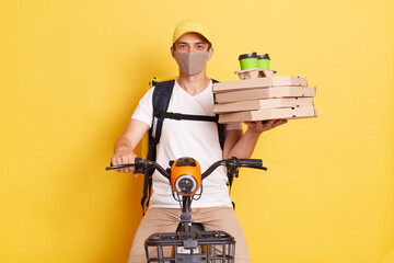 Deliveryman wearing protective mask holding pizza boxes and coffee from restaurant and riding...