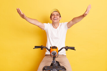 Extremely happy Caucasian young man wearing white t shirt and cap, riding electric bike and...