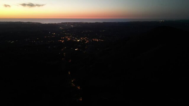 Town of Ascain France at dusk with artificial lights illuminating the near the Atlantic Ocean, Aerial flyover shot