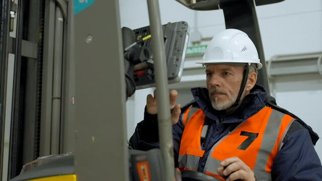 Bearded engineer sits in forklift cabin pushing button on monitor. Man in uniform checks condition of equipment in storehouse closeup slow motion