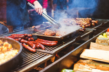 Outdoor street food festival. Chief cooking sausages, meat and potatoes cooking on an outdoor griddle