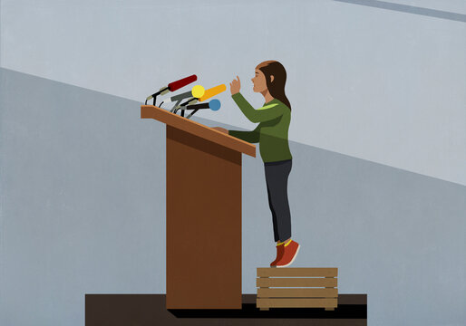 Girl standing on crate speaking at podium with microphones
