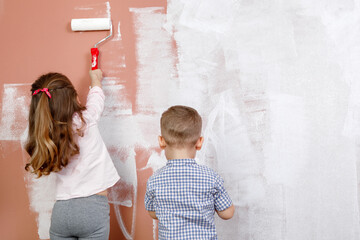 Little beautiful and happy child paint the wall with brush at home