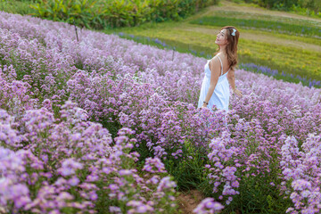 Young beautiful woman wearing  white dress relaxing in aromatic flowers field.