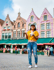 Fototapeta premium Women on a city trip in Brugge eating a Belgium waffle, the colorful house in the old city of Brugge with restaurants at the square. 