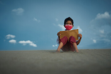 Little Boy sitting and reading book at the beach under blue sky