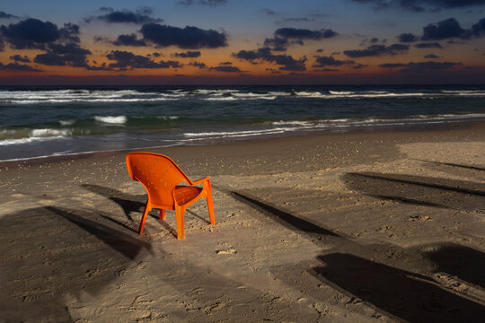 Orange lawn chair on sandy beach at dusk, Bat Yam, Israel

