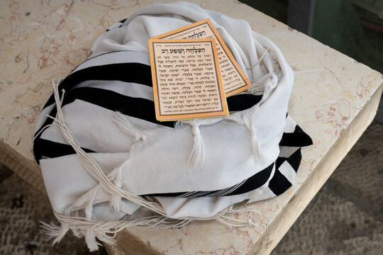 A tallit Jewish prayer shawl folded up on a bench with a booklet containing the text for a prayer for success and prosperity.