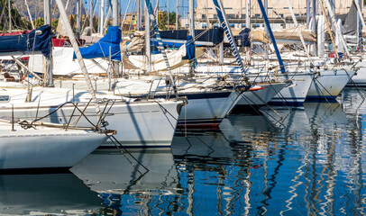 boats and yachts on pier in marine city port with masts and bulidings and blue sky on background